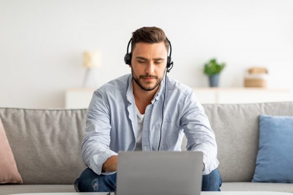 Hotline support service. Millennial male call center operator in headset working with laptop at home